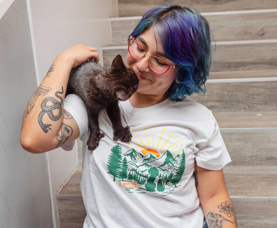 A black kitten on the shoulder of a smiling person wearing a Best Friends T-shirt