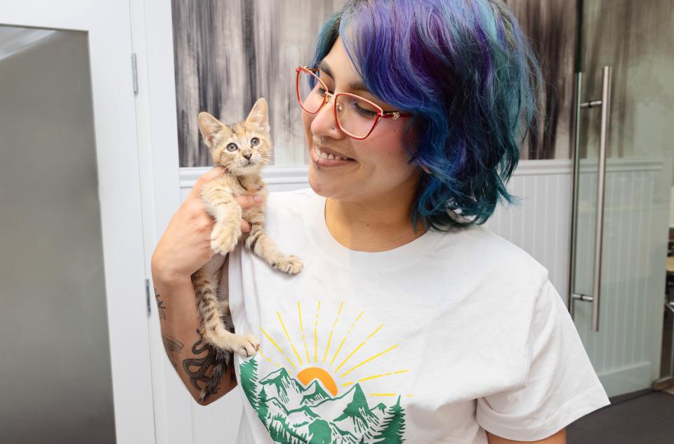 Smiling person holding a tiny kitten close to them