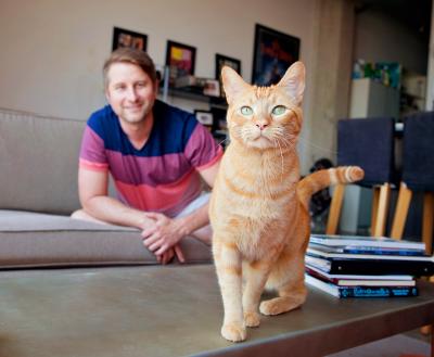 Smiling person sitting with an orange cat in a living room