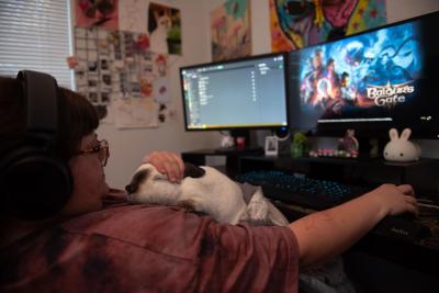 Keala gaming on a computer screen with Peter the rabbit lying on her chest with her petting him with one hand