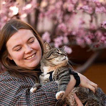 Person holding cat outside of pink flowering tree