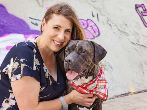 Smiling person hugging a dog whose tongue is out and is wearing a bandana