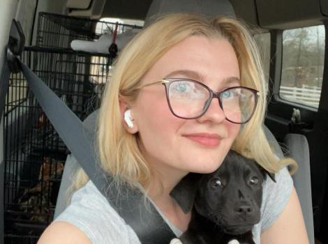 Emily Hirtle in a vehicle holding a small black puppy with a gloved hand