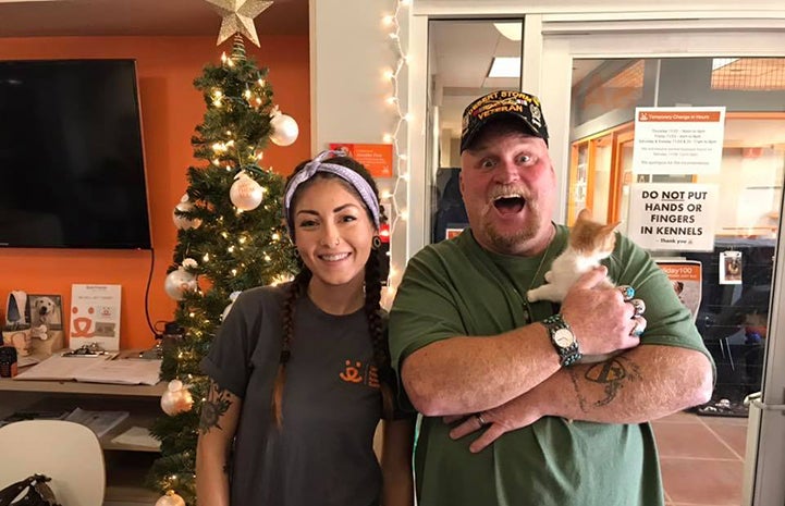 Excited man holding Ephiphany, the orange and white kitten he'd adopted, standing next to a Best Friends employee
