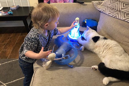 Russell the cat lying on the couch next to a toddler who is playing with a doll that lights up