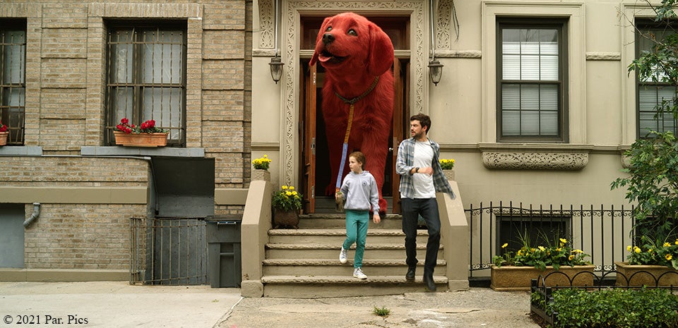 Clifford the Big Red dog walking on a leash out of a door with two people with copyright