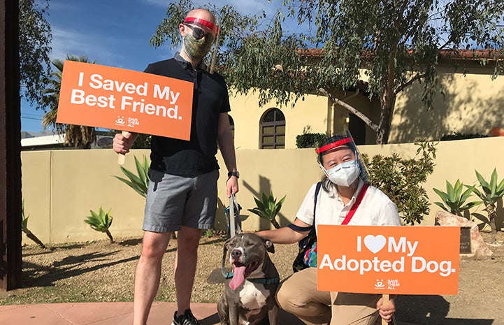 Two people holding signs, saying "I saved my best friend" and "I heart my adopted dog" while next to Cannoli the dog