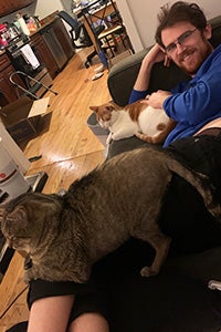 Man lying on a couch with Levi and Hank the cats