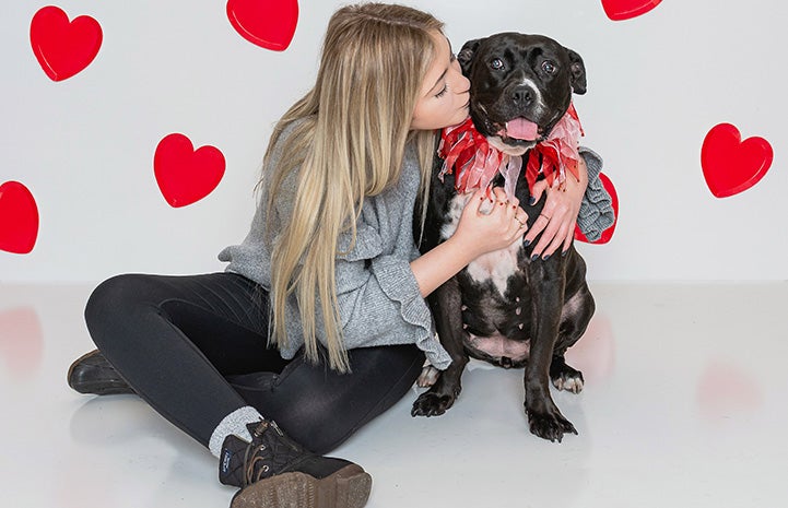 A woman kissing Jellybean, a black and white dog surrounded by red hearts