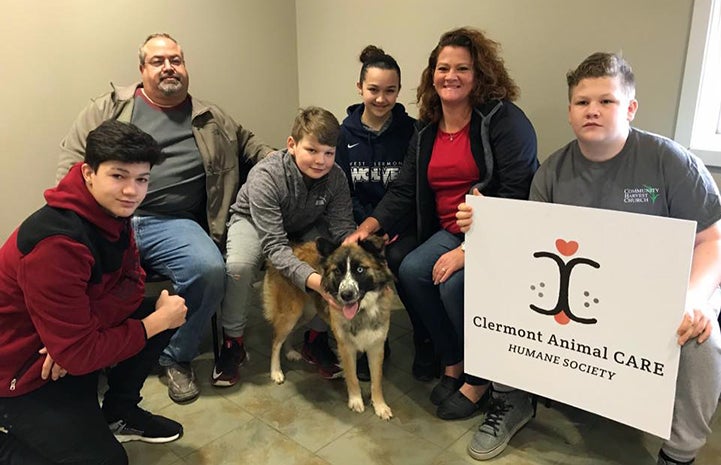 Family posing with an odd-eyed dog while holding a Clermont Animal CARE Humane Society sign