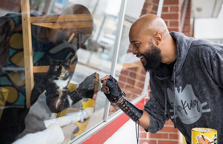 Sterling “Trap King” Davis looking in a window at a calico cat