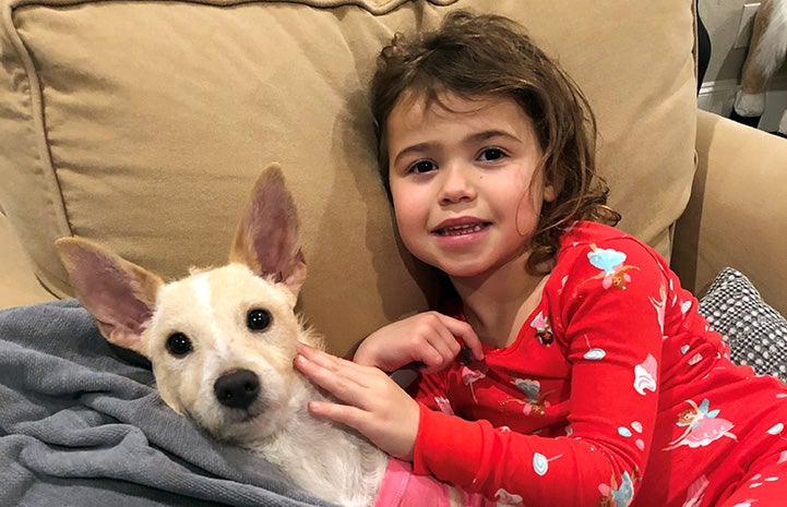 Young girl wearing pajamas lying on a couch next to Trudy the terrier