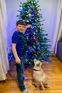 Young boy JP with Kash the dog in front of a decorated Christmas tree