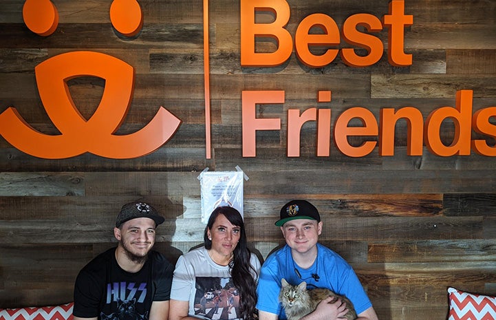 Boone the cat with his newly adopted family with a Best Friends sign and logo behind them