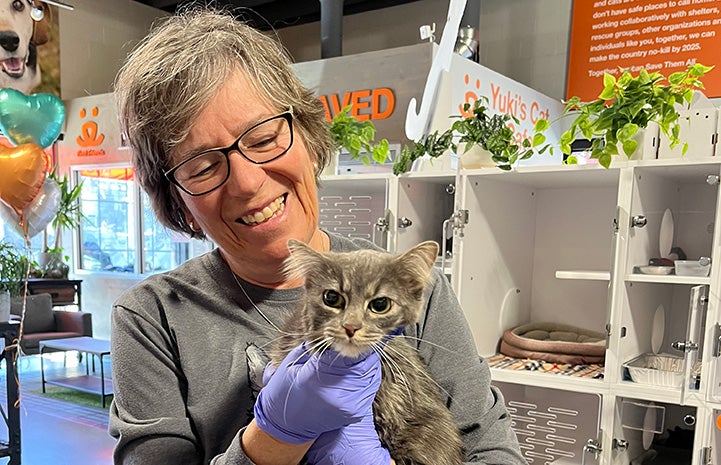 Volunteer Tana Hunter smiling and holding a gray tabby cat