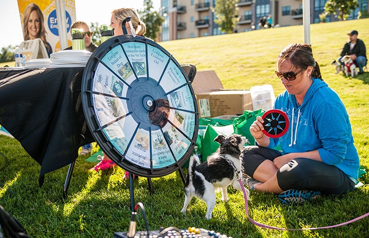 Woman with dog spinning a prize wheel at Strut Your Mutt