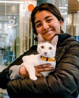 Woman in black coat holding white and tabby cat