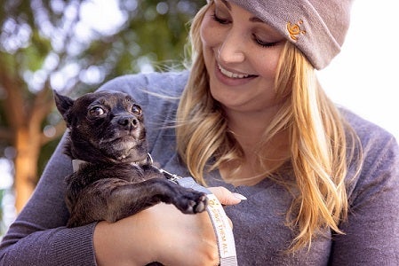 Woman holding and kissing small black dog