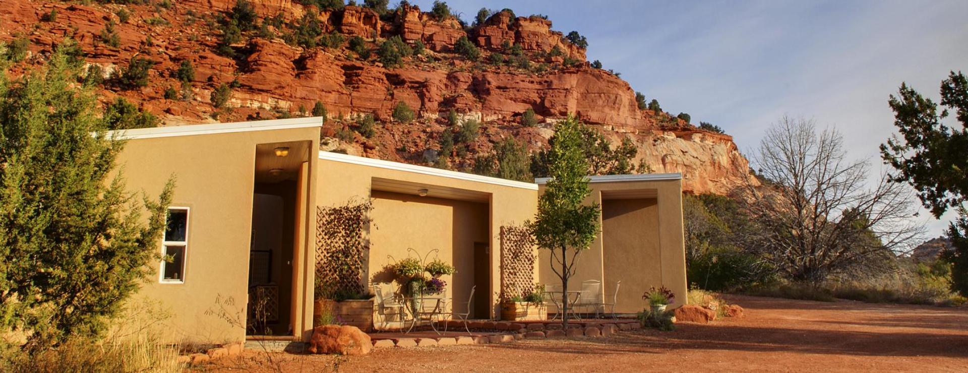 Small tan building in the desert with a backdrop of red rock cliffs and blue sky