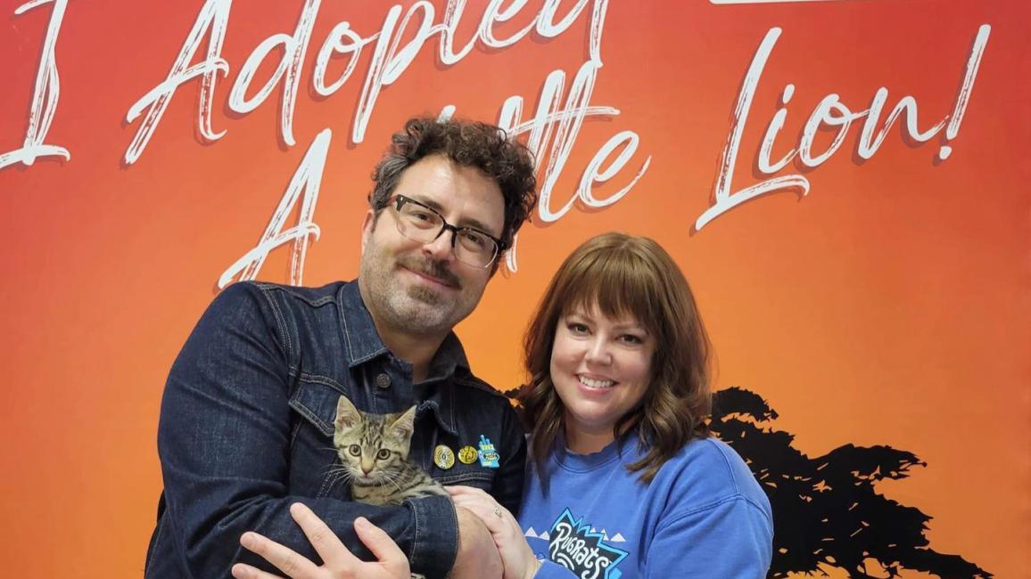 Couple adopting a kitten from Little Lion Foundation in front of a backdrop that says I adopted a Little Lion