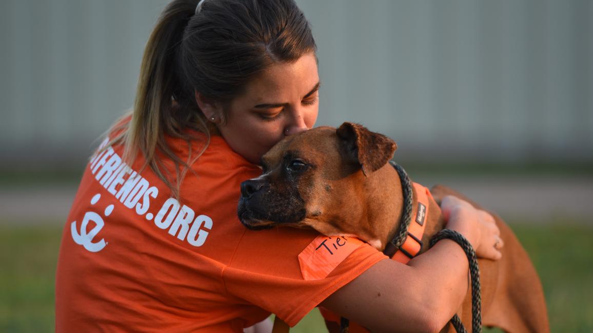 Best Friends caregiver hugging a boxer dog