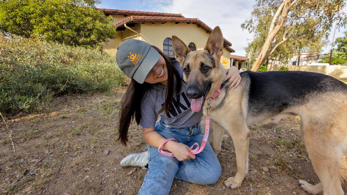 Person wearing Best Friends hat, hugging a German shepherd, by the Mission Hills location