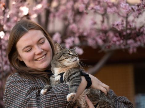 Caregiver Ashley McDaniel holding a cat in front of a flowering tree