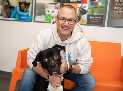 Volunteer Jeff Harris sitting on an orange seat hugging a black and white dog in front of him